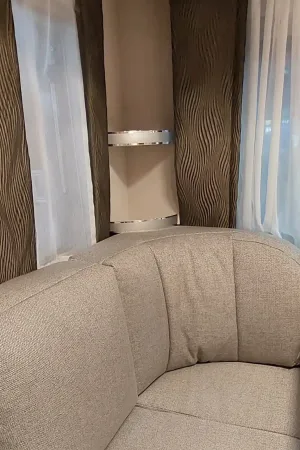 Vorhänge mit wellenartiger Struktur in dunklem Braun, kombiniert mit transparenten weißen Gardinen hinter einer Sitzecke in Grau